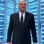 Kevin O’Leary (Mr. Wonderful) standing confidently in front of a massive futuristic data center with glowing servers, AI icons, and a subtle Shark Tank shark‑fin motif in sleek blues and silvers.